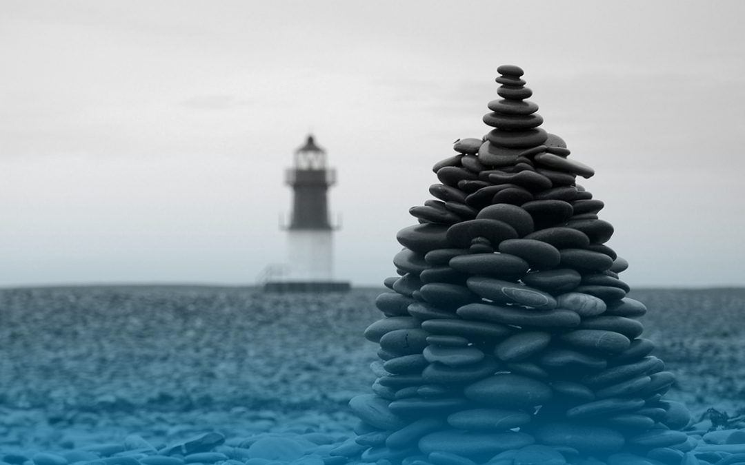 a pile of stones on the beach; a lighthouse in the backround; black and white; location: Isle of Man